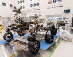 NASA's Perseverance six-wheeled rover pictured in a clean-room testing facility before launch, with engineers nearby.