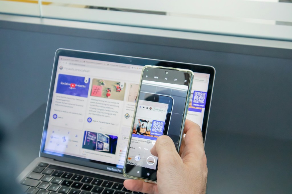 노트북 화면의 QR 코드를 스마트폰으로 촬영하는 사람의 손