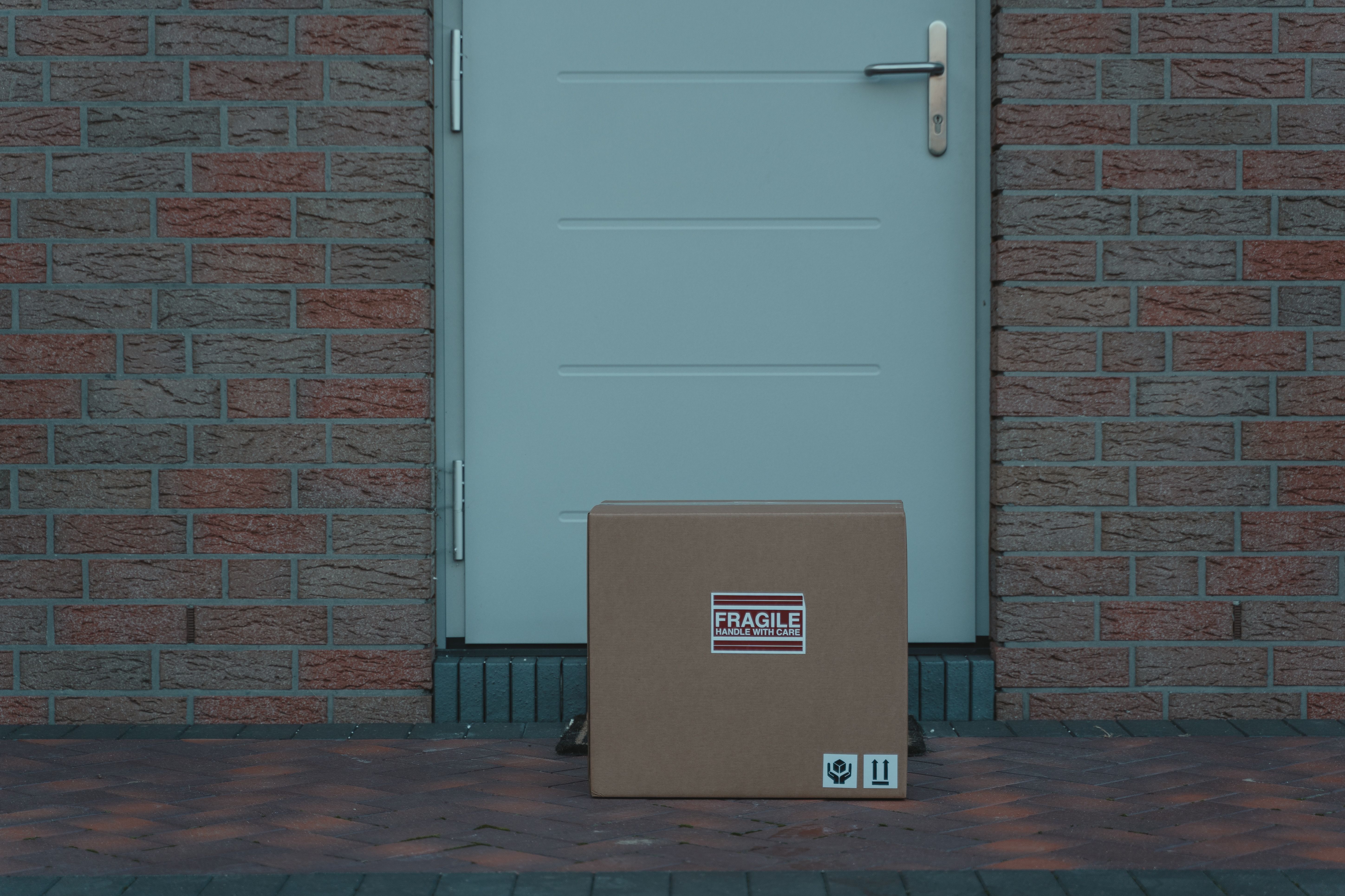 Illustrative brown cardboard package beside a residential doorway